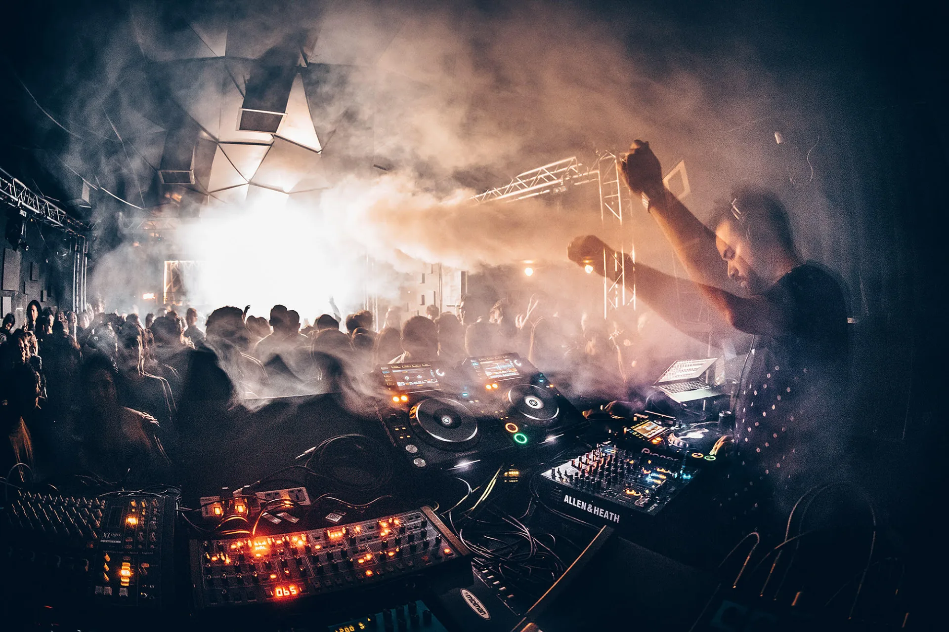 Spin in the booth, arm raised, facing a smoke-filled dance floor